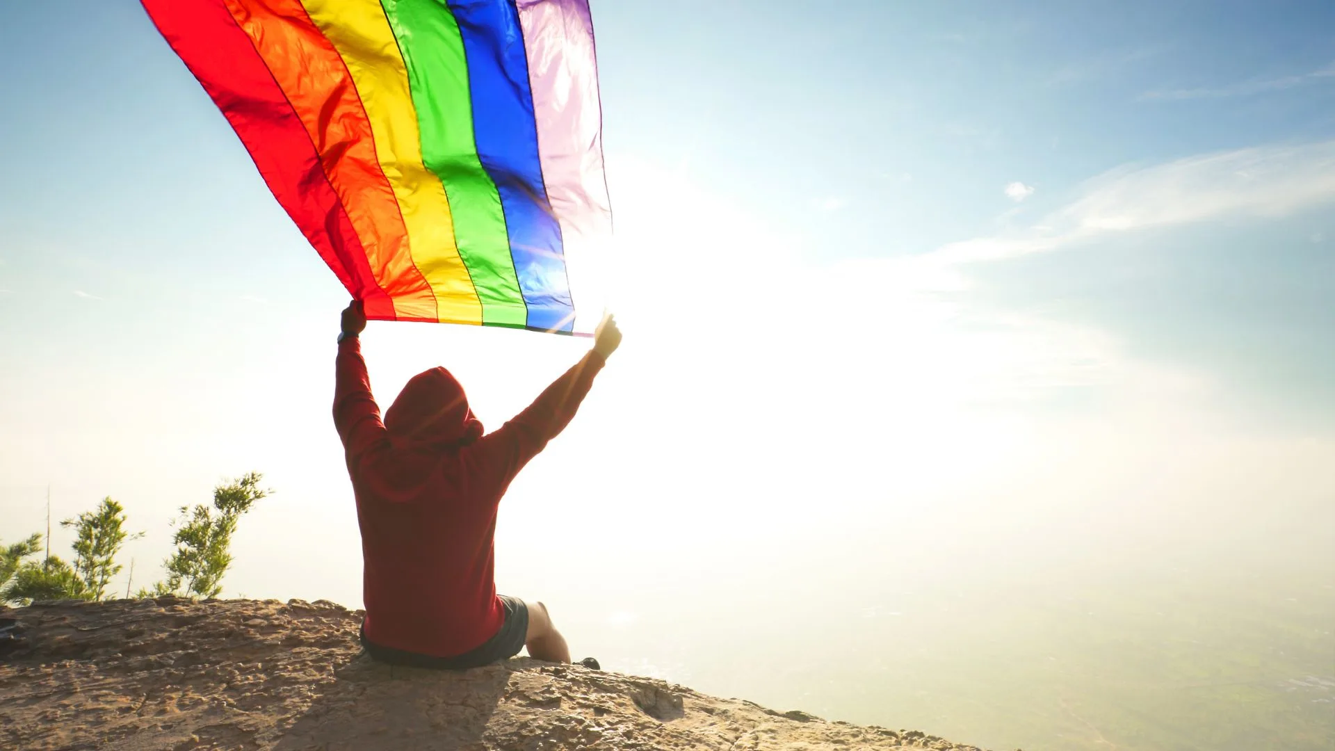 man raising the LGBT flag to the sky